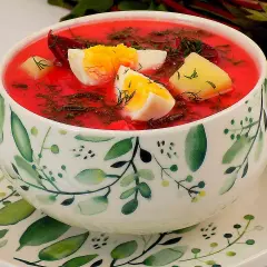Zupa z botwiny z ziemniakami i jajkiem, ozdobiona koperkiem, w miseczce z motywem roślinnym.