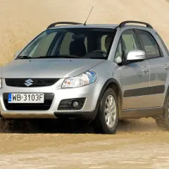 Srebrny Suzuki SX4 1.6 benzyna pokonuje piaszczystą wydmę, wzbijając tumany piasku.