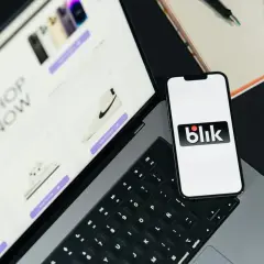 Na ekranie telefonu widnieje logo Blik. Obok leży tablet z ofertą zakupów online, pokazujący buty i elektronikę. Takie dane widzi odbiorca przelewu na telefon.