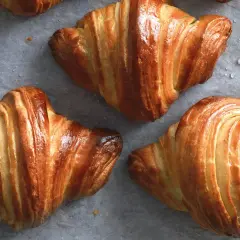Croissant dorati e sfogliati, perfetti per una ricetta croissant fatta in casa. Si intravedono gocce d'acqua sulla carta da forno.