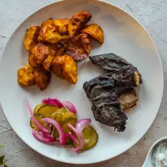 Talerz z pieczonymi ziemniakami, rybą i ogórkami kiszonymi.