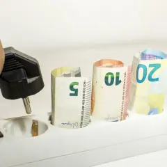 Dłoń z wtyczką, banknoty 5, 10, 20 euro w gniazdkach. Zastanawiasz się, jak zmienić dostawcę energii, by oszczędzać?