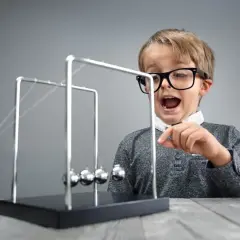 Chłopiec w okularach z otwartymi ustami obserwuje wahadło Newtona.