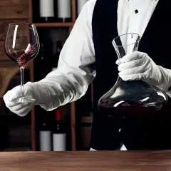 Kellner mit Handschuhen hält Weinglas und Karaffe. Eine Flasche Wein ergibt etwa 5 Gläser.