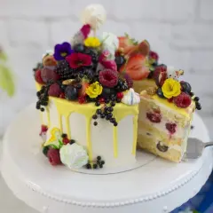 Wyjątkowy jesienny tort udekorowany świeżymi owocami, kwiatami i bezami. Kawałek ciasta już czeka na widelcu.