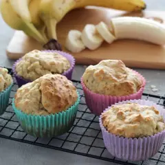 Fünf leckere Muffins ohne Zucker in bunten Förmchen, daneben Bananen und eine Schüssel Mehl.