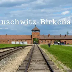 Brama obozu Auschwitz-Birkenau, gdzie jest to miejsce pamięci. Tłum zwiedzających podąża torami kolejowymi.