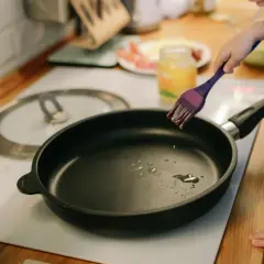 Dziecko smaruje patelnię olejem, przygotowując ją do smażenia. Zastanawiasz się, jaka patelnia najzdrowsza?