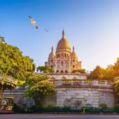 Sacre Coeur reser sig majestätiskt mot en klarblå himmel, med en karusell i förgrunden och en mås som svävar ovanför.