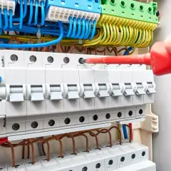 Instalacja uzbrojenia rozdzielni elektrycznej. Ręka z czerwonym śrubokrętem dokręca śrubę. Sprawdź uzbrojenie rozdzielni elektrycznej cena.