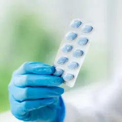 Ręka w niebieskiej rękawiczce trzyma opakowanie z niebieskimi tabletkami, które mogą pomóc w problemach z potencją.