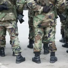 Żołnierze w mundurach moro, z karabinami, stoją w zwartym szyku. Ich buty i stopnie wojskowe są widoczne.