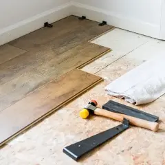 Laying LVP flooring parallel to the longest wall is a common practice. Tools like a rubber mallet and pry bar are ready for installation.