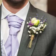 Elegancka butonierka co to? To ozdoba z kwiatów i lawendy przypięta do marynarki.