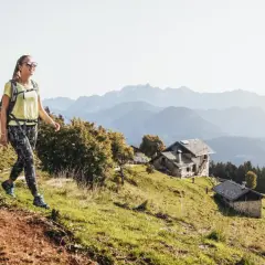 Para idzie na trekking po górach. W tle widać chatki i pasma górskie.