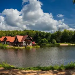 Idealne miejsce na długi weekend w sierpniu: urokliwe domki nad jeziorem, otoczone lasem, z pięknym niebem i chmurami.