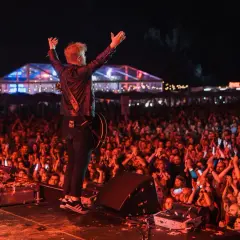 Artysta z podniesionymi rękami na scenie podczas koncertu. Tłum wiwatuje, tworząc niezapomniany line up Męskiego Grania.
