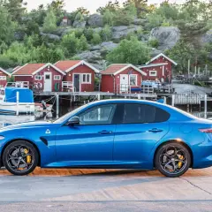 Blå sportbil vid en svensk hamn med röda sjöbodar. Undrar hur långt har bilen gått på denna vackra resa?