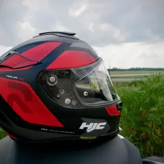 Kask motocyklowy HJC RPHA 70 w czerwono-czarne wzory, gotowy na przygodę na tle zieleni i nieba.