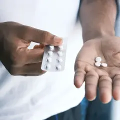 Dłoń trzyma blister z tabletkami, a na drugiej dłoni leżą trzy białe pigułki. Skudexa na co? Na ból głowy, gorączkę, czy inne dolegliwości.
