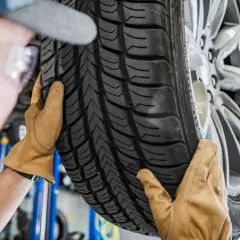 Mechanik w rękawiczkach ogląda bieżnik nowej opony samochodowej.