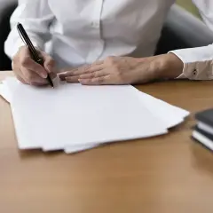 Dłoń pisze długopisem na białej kartce. Obok leżą notatniki. Szybka parafka i do dzieła!