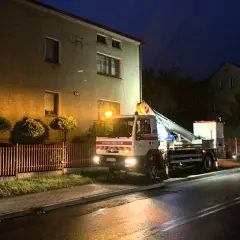 Samochód Tauron z podnośnikiem przy budynku, nocą. Zgłoszenie awarii w toku.