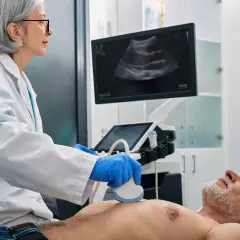 Ärztin führt Ultraschalluntersuchung durch. Der Bildschirm zeigt ein Bild, das auf eine Untersuchung von Organen oder Lymphknoten hindeutet.
