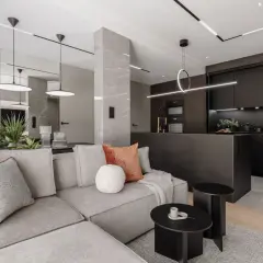 Nowoczesny salon z kuchnią, gdzie oświetlenie wpuszczane tworzy elegancką atmosferę. Szara sofa, czarne meble kuchenne i marmurowe detale.
