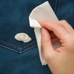 Jak usunąć gumę do żucia z ubrania? Dłoń z papierowym ręcznikiem próbuje zebrać gumę z dżinsowej kieszeni.