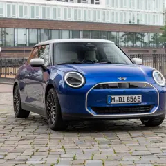 Mini Cooper SE azul aparcado en calle adoquinada, con edificios modernos de fondo. Su autonomía eléctrica inspira libertad.