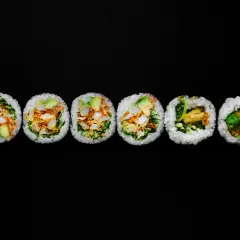 Sześć kawałków futomaki, czyli dużych rolek sushi, z awokado, warzywami i chrupiącym nadzieniem, ułożonych na czarnym tle.