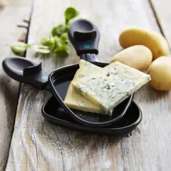 Tranches de bleu de Gex prêtes pour la raclette, avec des pommes de terre et de la verdure sur fond de bois.