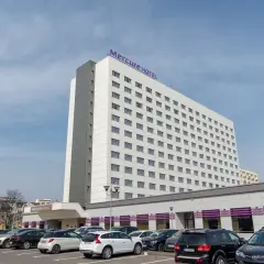Hotel Mercure Gdynia z parkingiem pełnym samochodów. Elegancki budynek hotelu góruje nad parkingiem.
