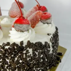 Tort udekorowany bitą śmietaną, czekoladą i mrożonymi wiśniami. Dowiedz się, jak przechowywać tort w lodówce, by zachował świeżość.