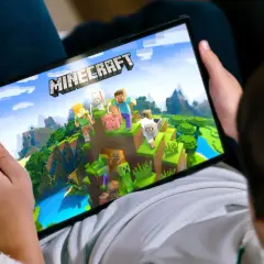 Dziecko gra na tablecie w Minecrafta, najpopularniejszą grę na świecie, eksplorując pikselowy świat z postaciami i zwierzętami.