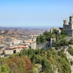 Widok na twierdze i miasto San Marino na wzgórzu, z pagórkowatym krajobrazem w tle.