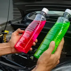 Manos sostienen botellas con líquido refrigerante de colores, rosa y verde, para el agua de motor coche.