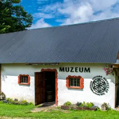 Muzeum w Bieszczadach zaprasza do odkrywania historii. Biały budynek z drewnianymi elementami i otwartymi drzwiami.