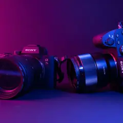 Dwa aparaty Sony, jeden z obiektywem 70-200mm, drugi z 85mm f/1.8. Różne rodzaje aparatów fotograficznych w neonowym świetle.