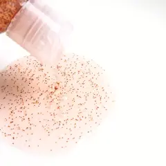 Przezroczysty żel z drobinkami, przypominający **mikroplastik w kosmetykach**, wypływa z butelki.