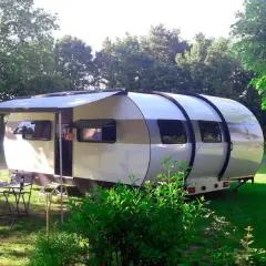 Une caravane XXL extensible, prête pour l'aventure, avec un auvent déployé et une table dressée sur l'herbe.