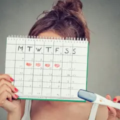 Donna con calendario segnato per il calcolo ovulazione e nidazione, tiene in mano un test di gravidanza.
