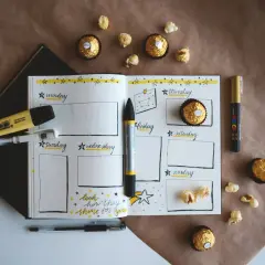 Plan rozwoju osobistego przykład: otwarty notatnik z kalendarzem tygodniowym, pisaki, czekoladki i popcorn.