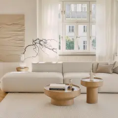 Jasny, przytulny salon z beżowym domem w tle. Miękka sofa, drewniane stoliki i subtelne dekoracje tworzą spokojną atmosferę.