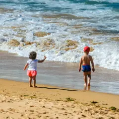 Dzieci w strojach kąpielowych dwuczęściowych dla dzieci bawią się na plaży, machając do fal.