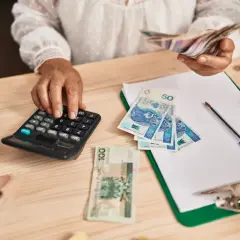 Kobieta liczy pieniądze na kalkulatorze, przygotowując się do rozliczeń związanych z samozatrudnieniem. Na stole leżą polskie banknoty.