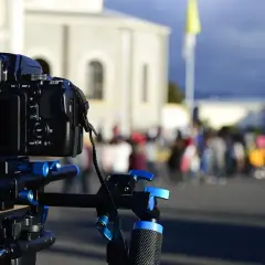 Kamera z matrycą pełnoklatkową na stabilnym statywie, gotowa do uchwycenia wydarzeń na tle rozmytego tłumu i budynków.