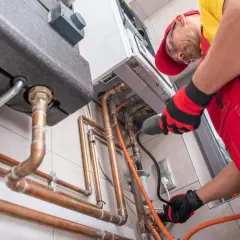 Un technicien installe une chaudière à gaz, une étape clé pour ma prime rénov. Il manipule des tuyaux en cuivre avec soin.