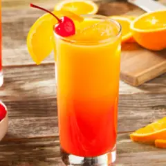 Cóctel refrescante con capas de granadina y naranja, adornado con una cereza y rodajas de naranja.